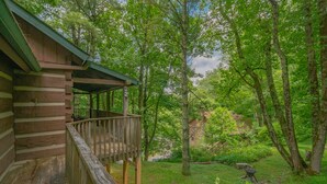 Eine Blockhütte mit einer Holzterrasse und einer Veranda, umgeben von üppiger Vegetation und Bäumen.