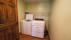 Un lavadero con una puerta de madera, lavadora y secadora apiladas, y un estante metálico sobre la secadora.