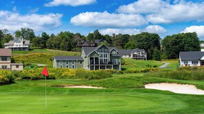 Um campo de golfe com um clube e várias casas ao fundo.