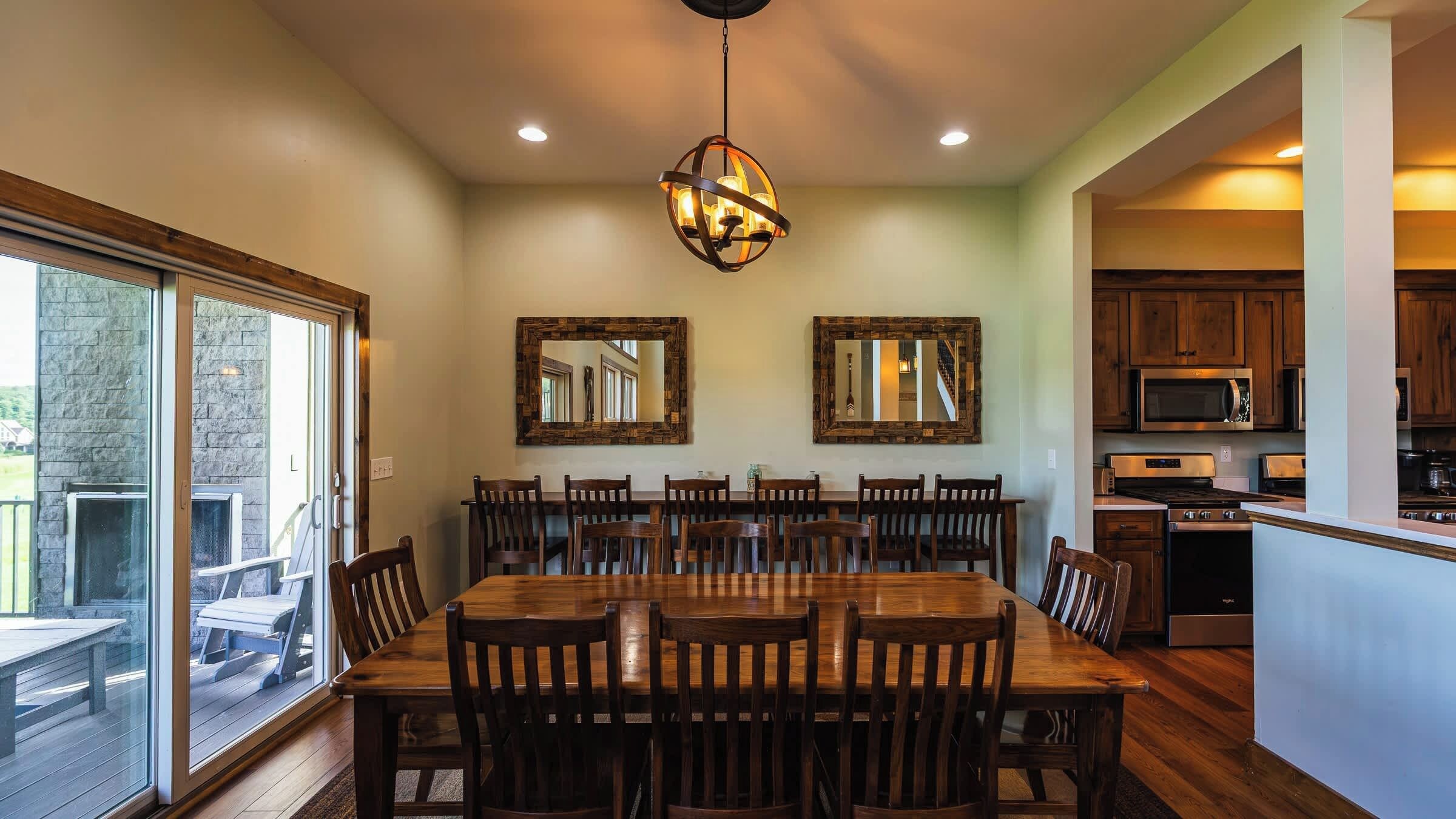 A dining area with a large wooden table and chairs, a hanging pendant light, and two wall-mounted mirrors.