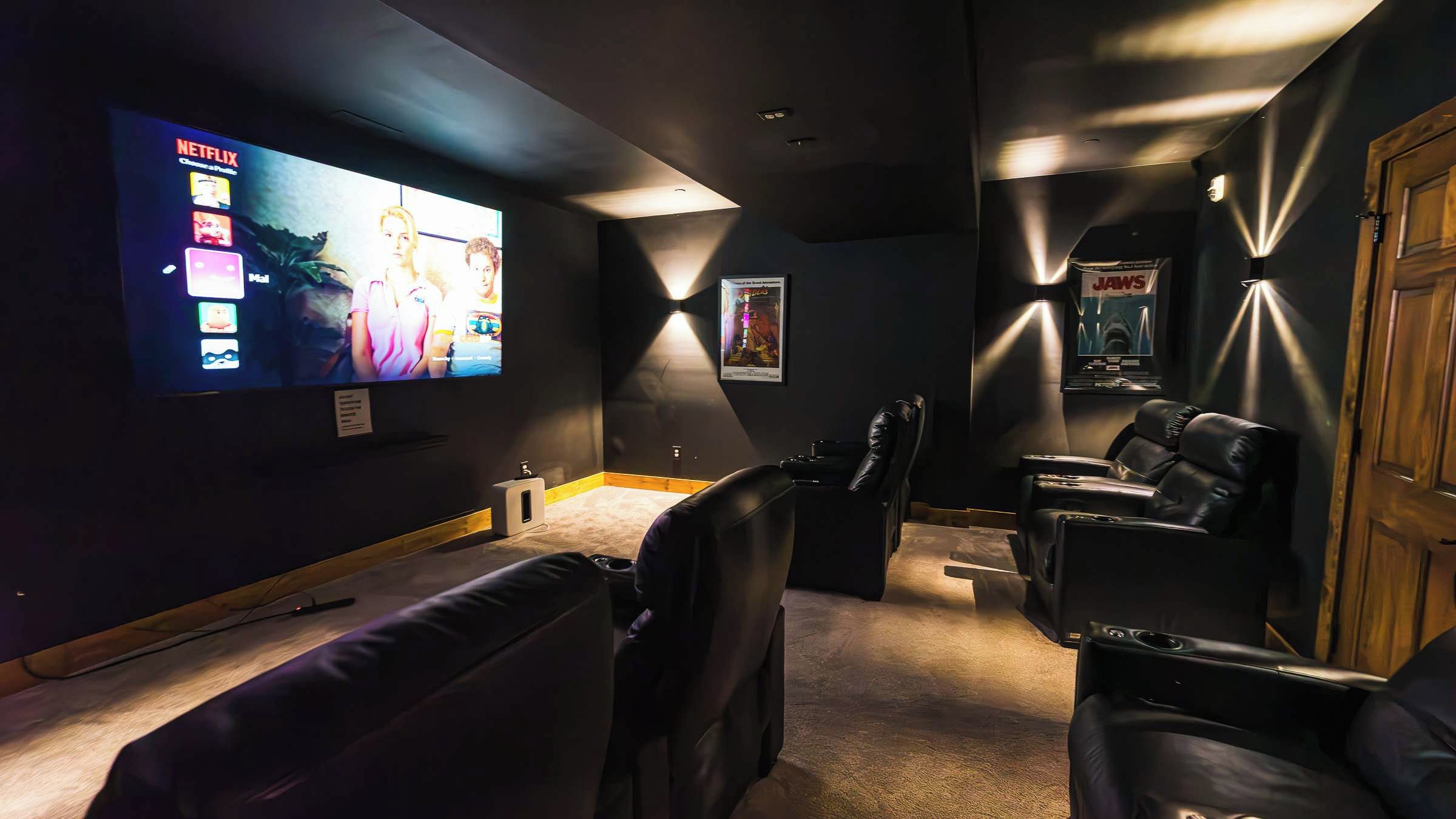 Une salle de cinéma maison équipée d’un grand téléviseur à écran plat, de plusieurs options d’assises, notamment un canapé et des fauteuils inclinables, et d’une porte en bois.