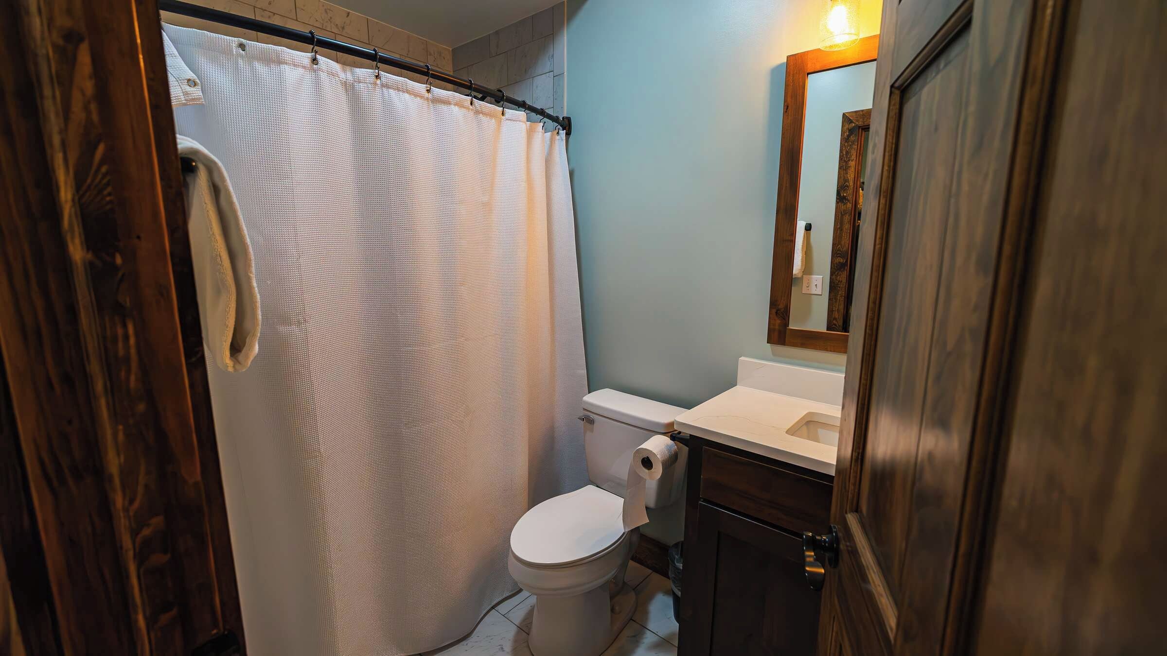 A bathroom with a shower curtain, toilet, sink, and a mirror.