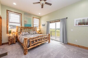 A bedroom with a rustic wooden bed, large windows, a balcony, and a ceiling fan. - Luxury Deep Creek Lake House w/ Pool & Theater (Deep Creek)