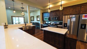 A modern kitchen with a large island, stainless steel appliances, wooden cabinets, and pendant lighting.