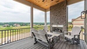 En overdækket terrasse med Adirondack-stole, en pejs i sten og udsigt over et grønt landskab.