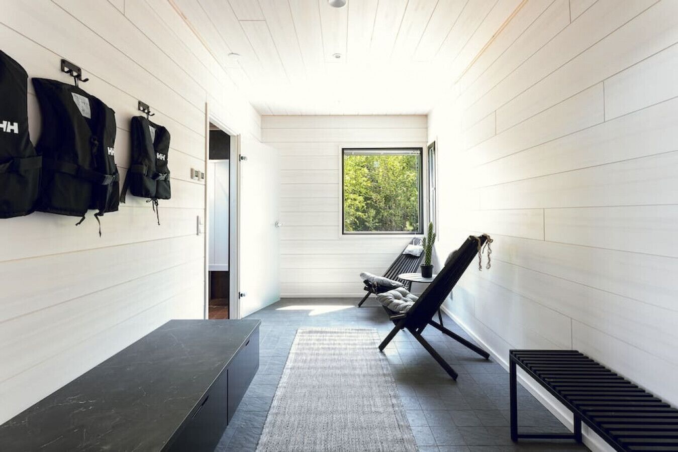 A modern, minimalist bathroom with a bench, a small table, and a window providing a view of greenery.