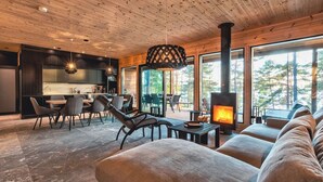 A modern interior with a wooden ceiling, a fireplace, and large windows offering a view of trees. - State of the Art Coastal Villa (Salo)