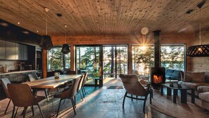 A modern interior with a wooden ceiling, a dining area, a fireplace, and large windows offering a view of trees. - State of the Art Coastal Villa (Salo)