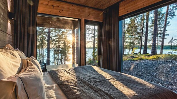 A bedroom with a large bed, wooden ceiling, and a view of a lake and trees. - State of the Art Coastal Villa (Salo)