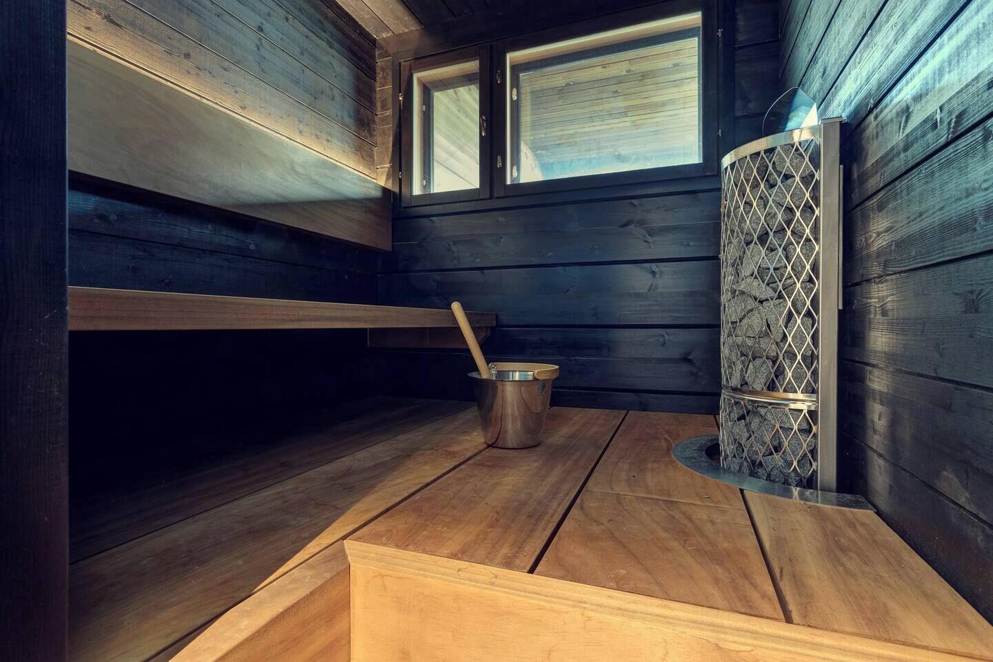 A sauna room with wooden walls, a bench, a bucket, and a window.
