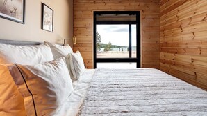 Un dormitorio con una cama grande, paredes de madera y vistas a una playa a través de una ventana.