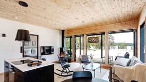 Un interior moderno con techo de madera, una zona de cocina, una mesa de comedor y un área de estar con vistas al exterior.