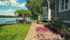 A lakeside property with a wooden dock, a grassy lawn, and a flower bed.