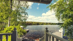 A wooden deck with a railing overlooking a lake, surrounded by trees and a clear sky.