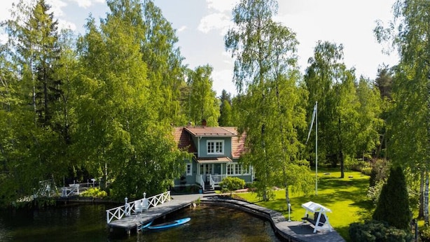 A house with a dock and a small boat, surrounded by trees and a grassy area.