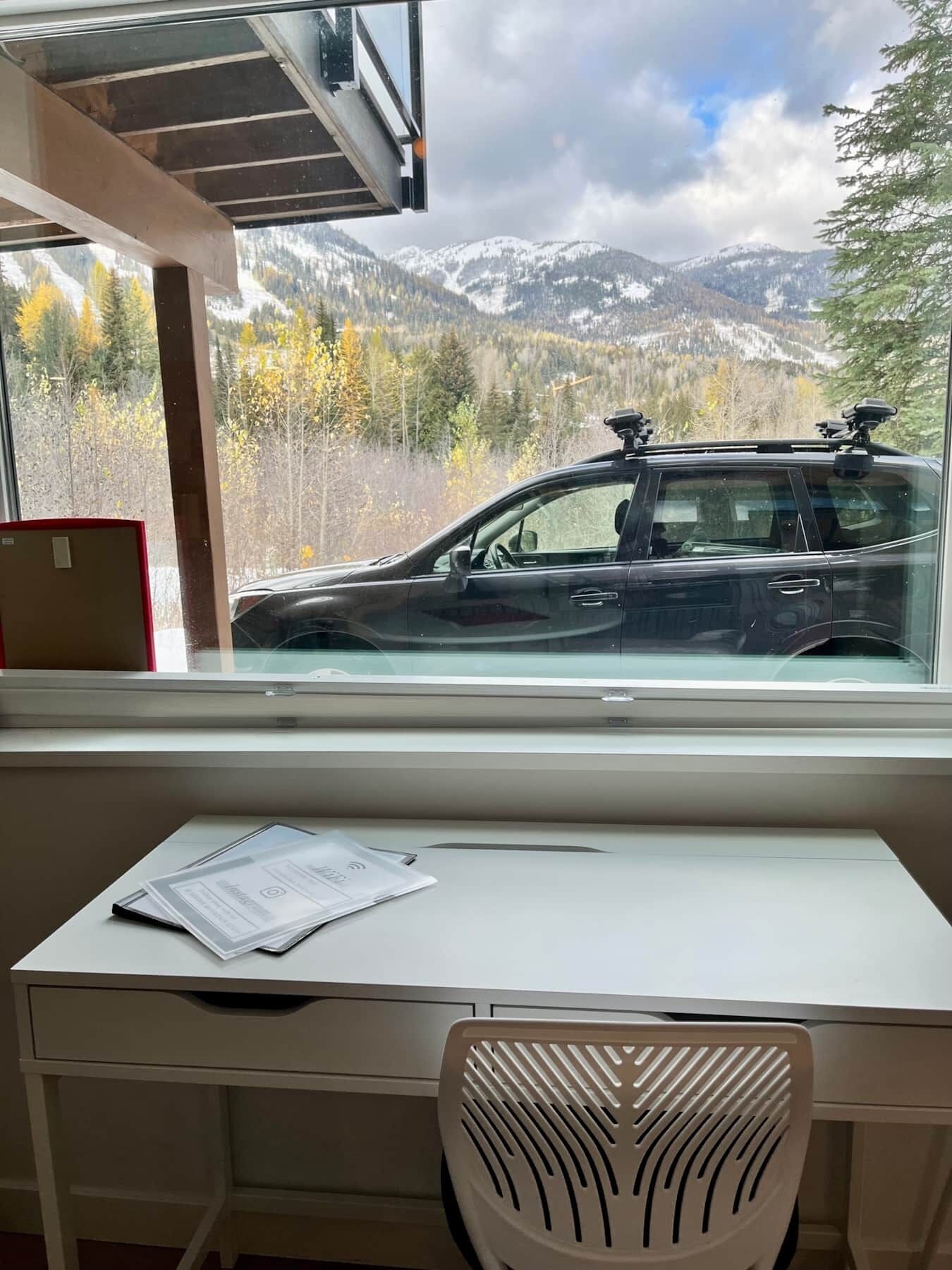 A room with a desk, chair, and a window overlooking a snowy mountain landscape.