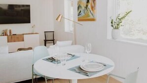 A modern, minimalist room with a round dining table, two chairs, a ceiling fan, a flat-screen TV, a painting, and a window with a plant. - Red Mtn Private Mountain Escape for Active Couples (Rossland)