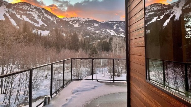 Een balkon met uitzicht op besneeuwde bergen en een ondergaande zon.