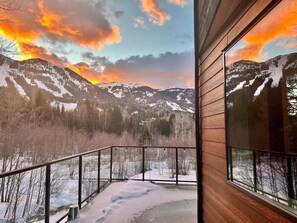 A balcony with a view of snow-covered mountains and a sunset. - 4BR Luxury Basecamp-All Seasons-Sauna-Steam-Soak (Rossland)