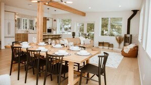 Een moderne eetruimte met een houten tafel voor zes personen, omringd door donkere stoelen. In de achtergrond is een keuken zichtbaar met een groot raam.