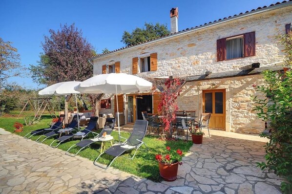 A stone building with a patio area featuring lounge chairs and umbrellas. - Villa Katherine with Pool and Game Room (Žminj)