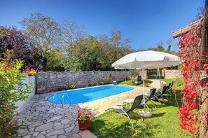 A backyard with a swimming pool, stone patio, and outdoor seating area with umbrellas. - Villa Katherine with Pool and Game Room (Žminj)