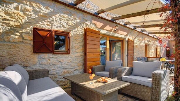 A stone-walled outdoor seating area with wicker furniture and a pergola.
