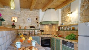 A kitchen with stone walls, wooden beams, a tiled backsplash, and a variety of kitchen appliances and utensils.