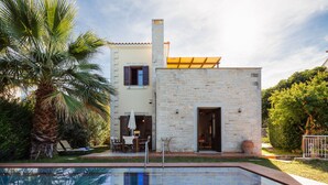 A two-story house with a stone facade, a pool, and a patio with outdoor furniture.