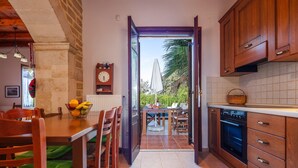 A kitchen with wooden cabinets, a dining table with chairs, and a view of the outdoors through an open door.