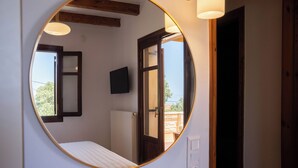 A bedroom with a round mirror, a bed, a television, and a door leading to an outdoor area.