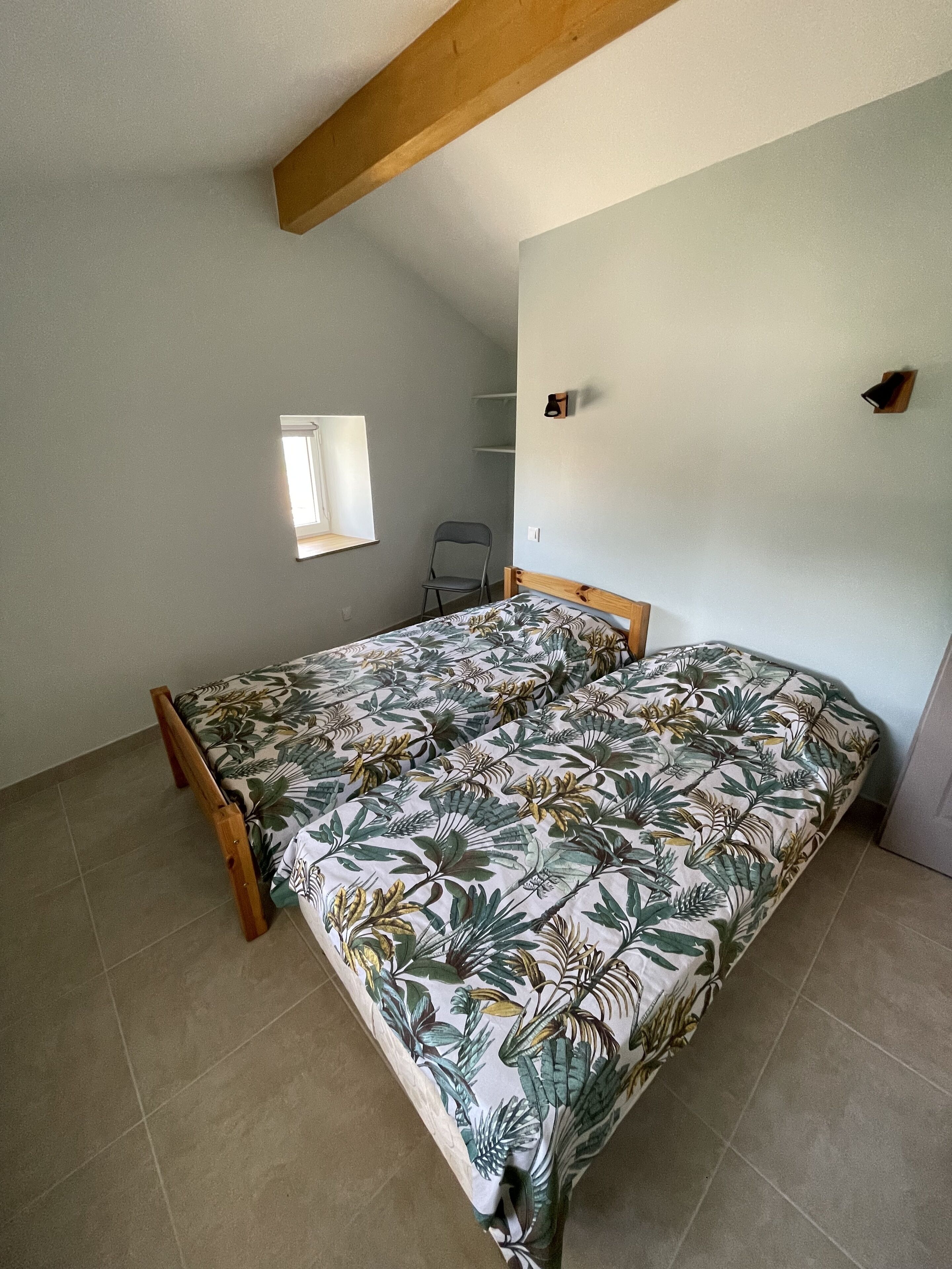 A bedroom with a bed, a chair, a window, and a shelf.
