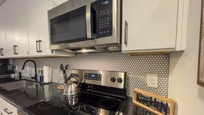 A modern kitchen with stainless steel appliances, a microwave, an induction cooktop, and a kettle. - Mid Century Modern Apartment w/ a pool! (Judson)