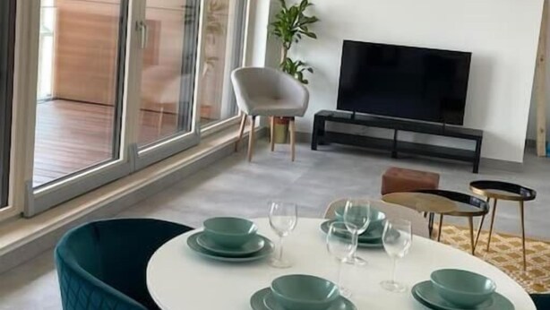 Un espace repas moderne avec une table ronde, des chaises de couleur turquoise et une grande fenêtre donnant sur l’extérieur.