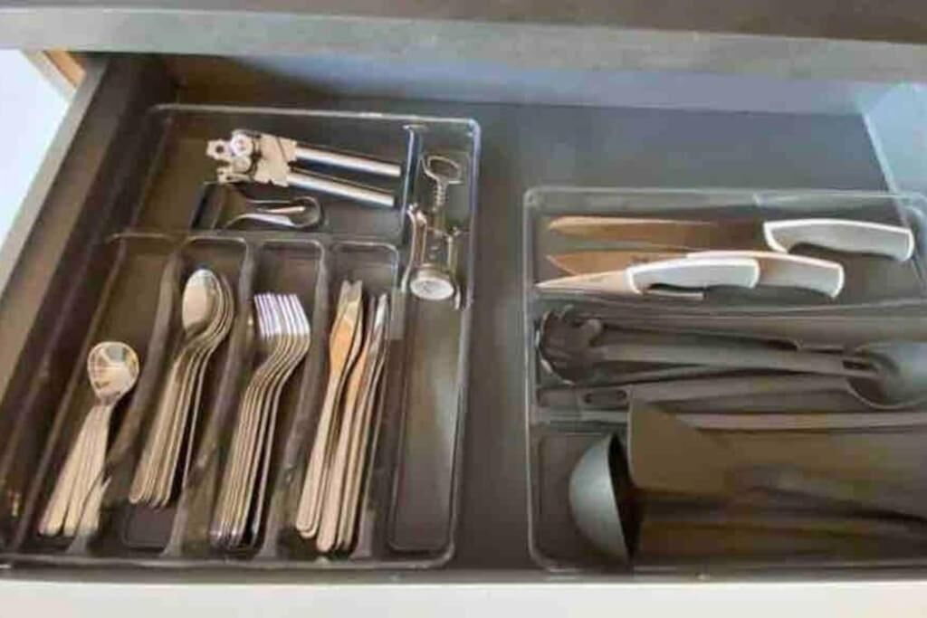 A drawer with compartments containing various utensils and tools, including forks, spoons, knives, and a pair of scissors.