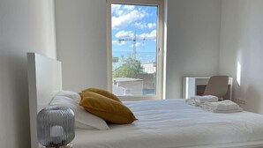 Une chambre d’hôtel avec un lit, une lampe de chevet, une chaise et une vue sur la mer et les bâtiments.
