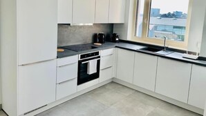 Une cuisine moderne avec des meubles blancs, un plan de travail noir et une fenêtre donnant sur la ville.