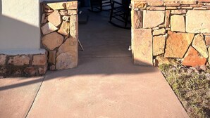 Un patio cubierto con paredes de piedra, suelo de concreto y dos mecedoras.