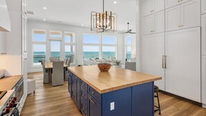Una cocina moderna con una isla grande, armarios blancos y vista al océano.