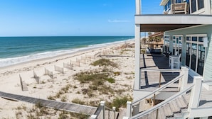 Una propiedad frente a la playa con terraza de madera, balcón con mobiliario exterior y vista al océano.
