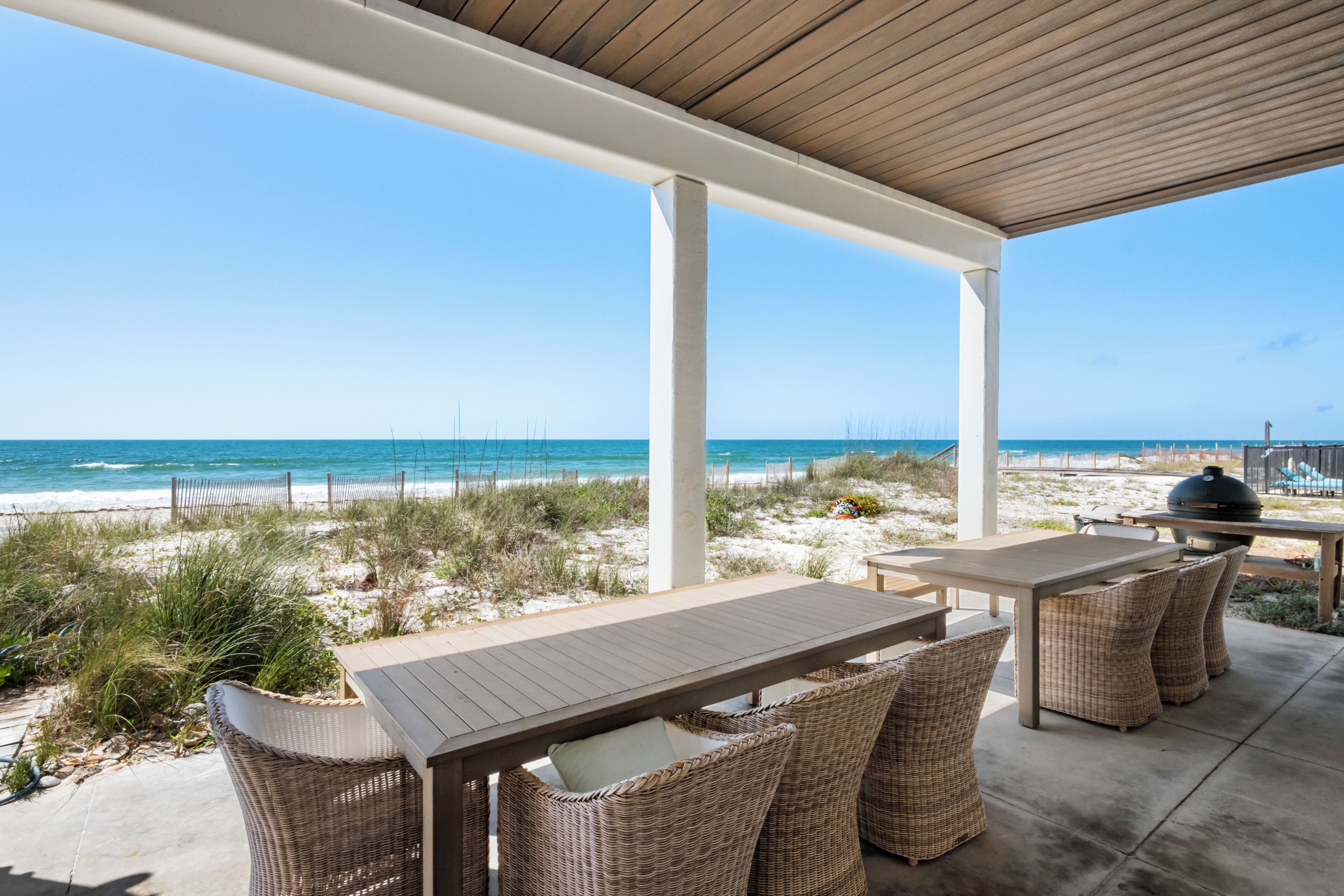 Un espacio al aire libre techado con vista a la playa, que incluye una mesa y sillas de mimbre.