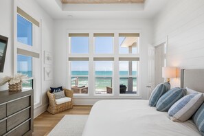 Une chambre avec une grande fenêtre, un lit, une commode, une chaise et une lampe.