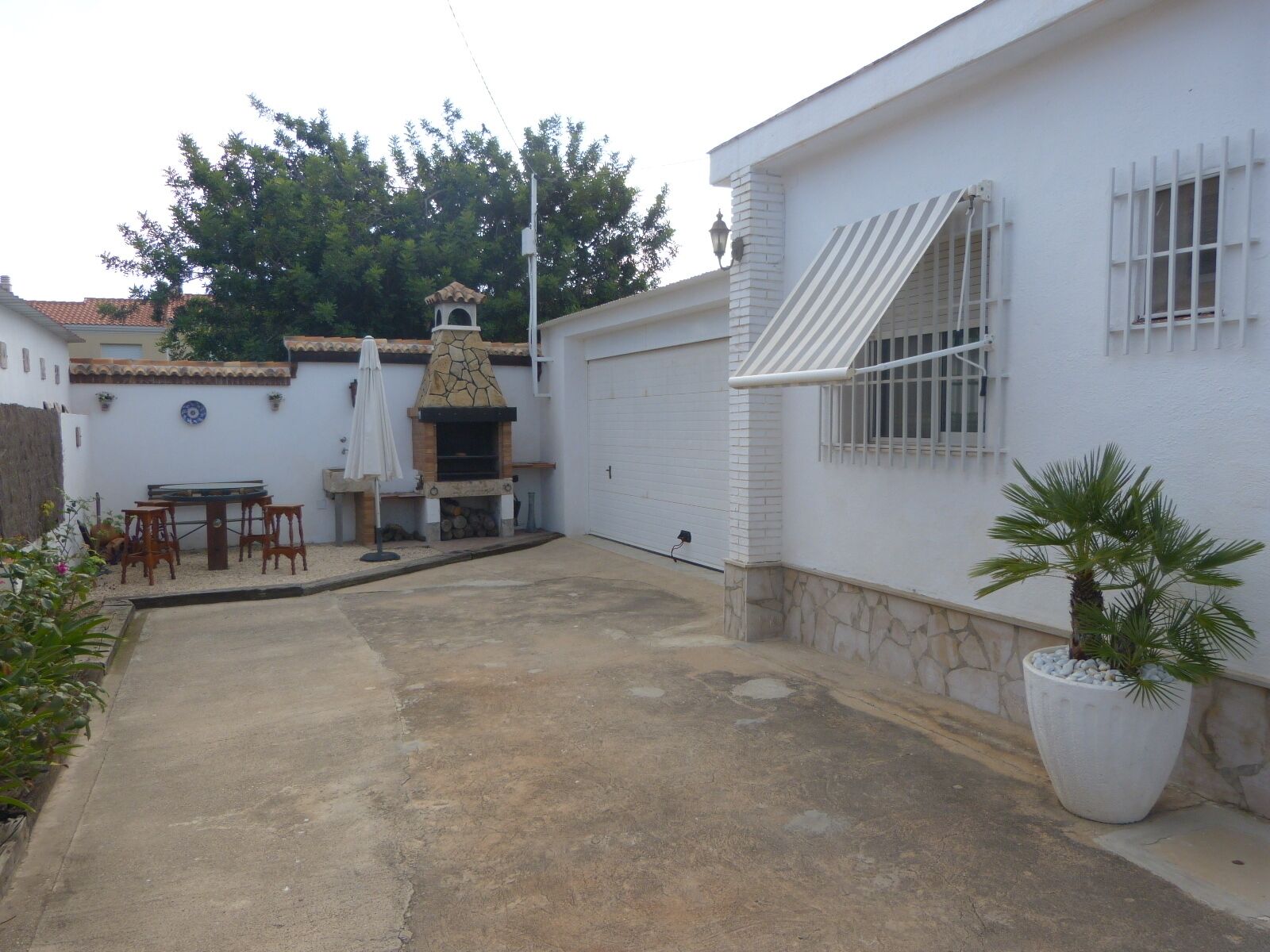 Un patio con chimenea de piedra, mobiliario exterior y una planta grande en maceta.