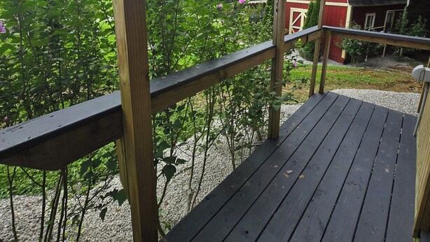 Una terraza de madera con vista a una casa roja y vegetación circundante.