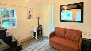 Una sala de estar acogedora con techo de madera, un escritorio blanco, una silla negra, un sofá marrón y un espejo que refleja la habitación.