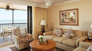 A hotel room with a balcony, a sofa set, a coffee table, and a painting of a tropical scene.