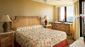 A hotel room with a large bed, a nightstand, a dresser, and a window with a view of the ocean.