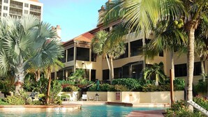 A pool area with palm trees and a building with balconies.