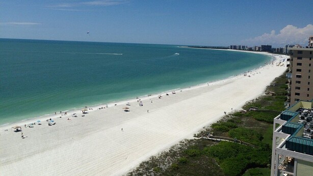 A beach with a white sandy shore, clear blue water, and a city skyline in the background.