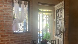 A dining area with a wooden table, metal chairs, a potted plant, and a view through a window with a white curtain. - De Casa Eu Gosto (Ubatuba)